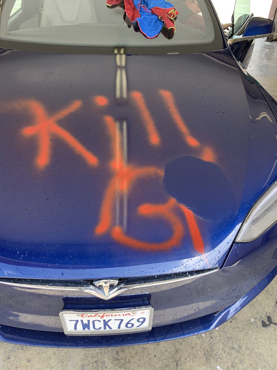 Blue Tesla Model S with red spray paint graffiti on the hood before specialty paint correction at Fair Oaks Car Wash